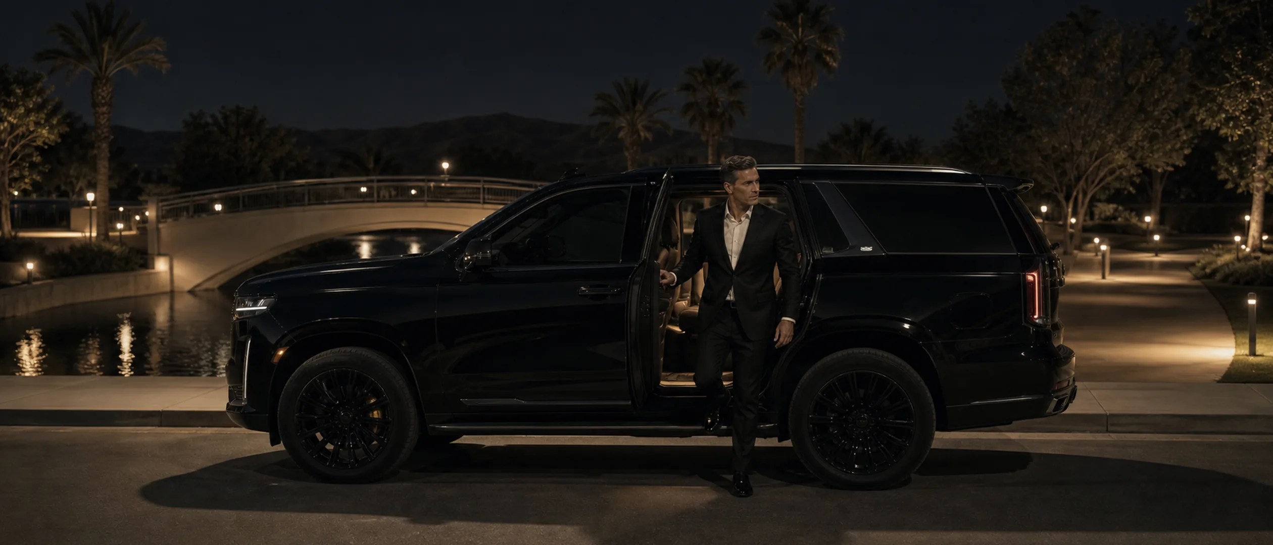 An executive steps from a black vehicle beside Mill Creek Park in Bakersfield at dusk.